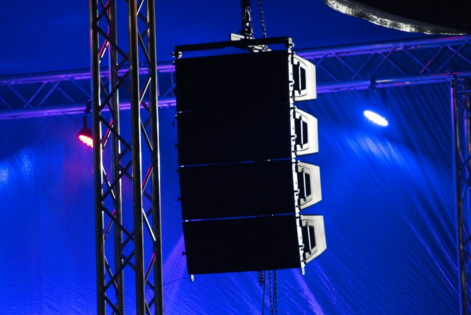 Altavoz activo montado sobre un pie junto a una mesa de mezclas en un evento